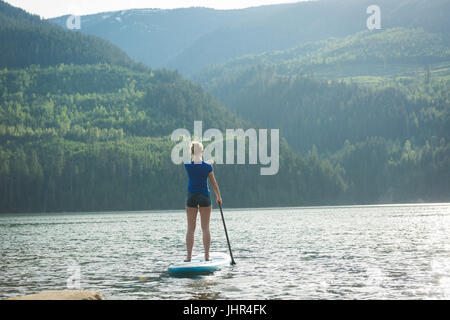 Vista posteriore della donna paddleboarding nel lago contro le montagne Foto Stock