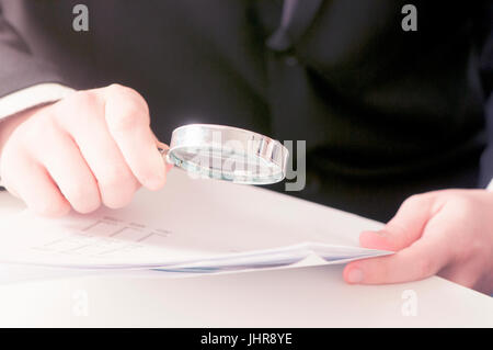 Close-up del giovane imprenditore esaminando mano fattura con lente di ingrandimento Foto Stock