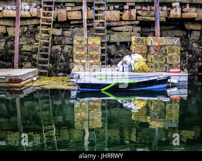 Una piccola barca legata a un dock impilati con filo lobster trappole in Rockport, Maine, Stati Uniti d'America. Foto Stock