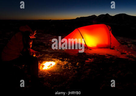 Uomo con falò e tenda illuminata, Engerdalsfjellet, sullo sfondo del vertice Rendalssoelen, Hedmark Fylke, Norvegia, ottobre 2011, Mann mit L Foto Stock