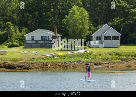 Case di mare sulla baia di Pemaquid e una donna paddleboarding nel villaggio di Porto Nuovo, Bristol, Maine, Stati Uniti d'America. Foto Stock