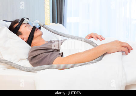 La mezza età uomo asiatico dormire nel suo letto indossando maschera CPAP per collegamento tubo flessibile aria, dispositivo per persone con apnea nel sonno Foto Stock