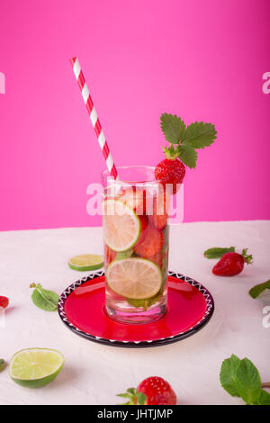 Limonata Fresca con fragole, lime e menta in un bicchiere alto su una bianca e sfondo rosa Foto Stock