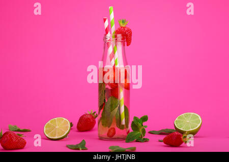 Limonata Fresca con fragole, lime e menta in un bicchiere alto su un sfondo rosa Foto Stock