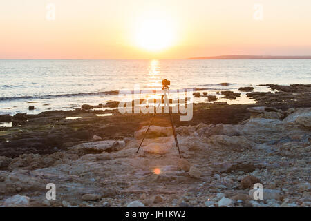 Fotocamera con treppiede oltre il sole che sorge nei pressi della spiaggia Foto Stock