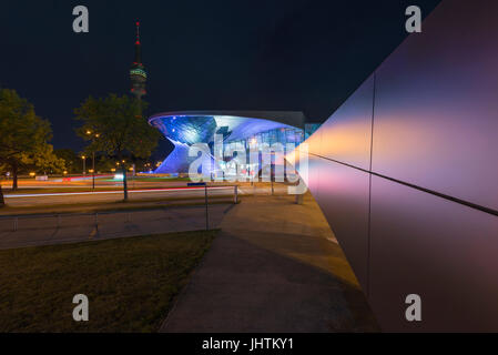 Architettura futuristica di una passerella verso la facciata illuminata del BMW Welt di Monaco di Notte Foto Stock