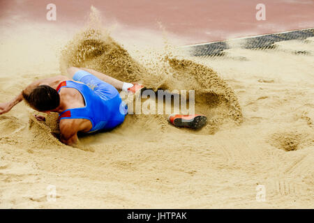 Atleta maschio salto in lungo lo sbarco a spruzzo di sabbia Foto Stock
