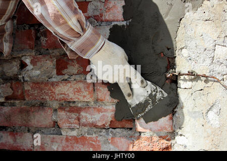 Un costruttore professionale muratore con cazzuola a mano si applica la malta di cemento per il muro di mattoni nella parte anteriore del rivestimento durante il restauro del sito nella parte anteriore del cinema Foto Stock