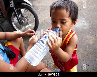 CAINTA City, Filippine - 12 luglio 2017: un ragazzo beve da una bottiglia mentre su un marciapiede. Foto Stock