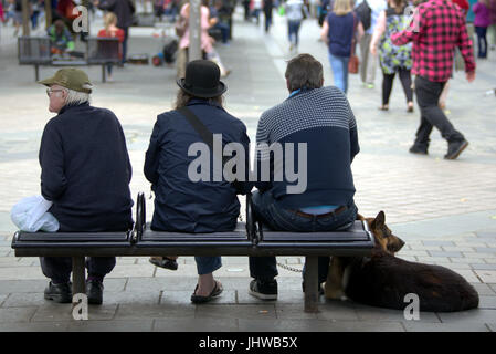 Tre individui maschi e un cane seduto su una panchina in Sauchiehall Street Glasgow Foto Stock