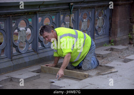 Pietre per pavimentazione posata sul ponte Partick cementer la posa di uno strato di fondazione costruzione edilizia lavoratore in alta viz camicia Foto Stock