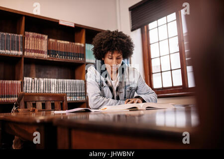 African studente di college la lettura di libro in biblioteca. Giovane studente seduto a tavola in libreria e studiare. Foto Stock