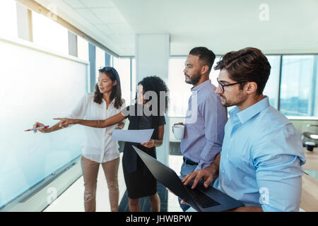 Le donne imprenditrici a discutere idee di business in sala riunioni con i loro colleghi. Giovani investitori aziendali presentando un piano aziendale su una lavagna bianca Foto Stock