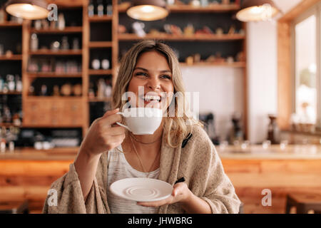 Ritratto di giovane e bella donna in piedi in un bar e bere il caffè. Sorridente giovane femmina presentando un caffè in un ristorante. Foto Stock