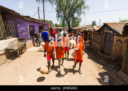 Bambini da Kibera Slum passeggiando per le stradine laterali con il calcio dopo la formazione, Nairobi, Kenia Foto Stock