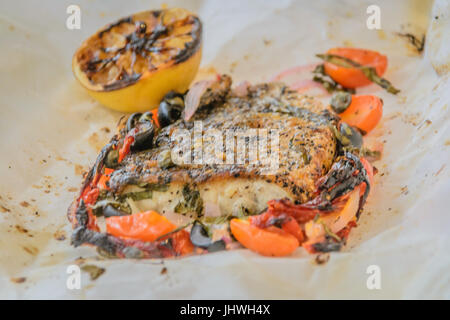 Branzino al cartoccio di mare fresca filetto di branzino cotto in carta pergamena con pomodori secchi, acciughe e capperi Foto Stock