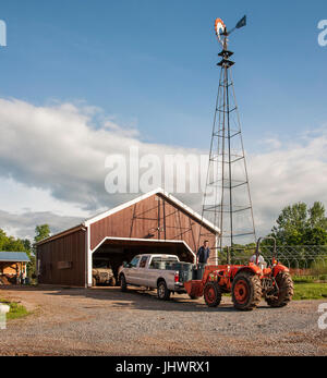 Gli agricoltori con il carrello di prelievo e il trattore nella parte anteriore del granaio rosso, nuvole nel cielo Foto Stock