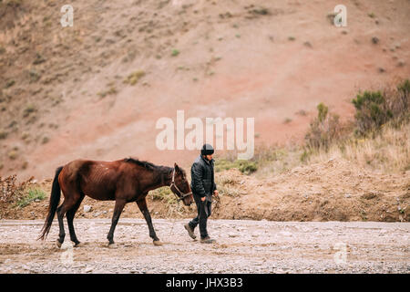 Sagarejo Comune, Regione di Kakheti, Georgia. L'uomo conduce vicino a Cavallo ortodosso georgiano David Gareja complesso del convento. Rocce Rosse nel deserto Gareja, kak Foto Stock