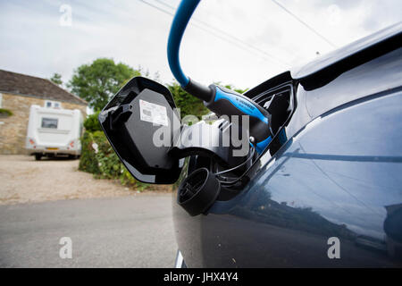 Un elctric auto e punto di caricamento parcheggiata sul lato della strada outsiude una casa con il cavo blu. Foto Stock