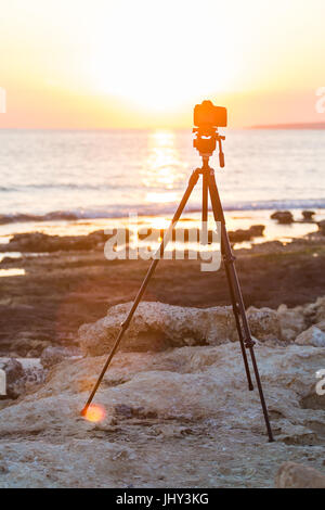 Fotocamera con treppiede oltre il sole che sorge nei pressi della spiaggia Foto Stock