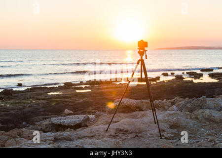 Fotocamera con treppiede oltre il sole che sorge nei pressi della spiaggia Foto Stock
