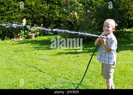 Piccolo Ragazzo gioca con tubo flessibile per acqua in giardino - se campana-boy gioca con un paio di pantaloni subito nelle protezioni, kleiner Junge spielt mit Wasserschlauch im G Foto Stock