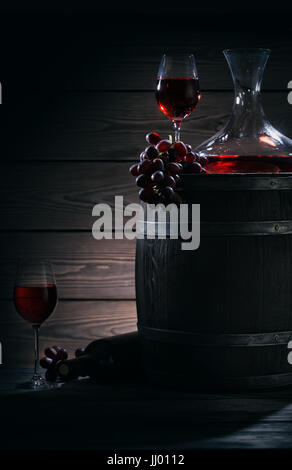 Barile, decanter e bicchieri di vino rosso in una cantina scuro. Ancora in vita su un tema di vino rosso. Luce magica. Foto Stock