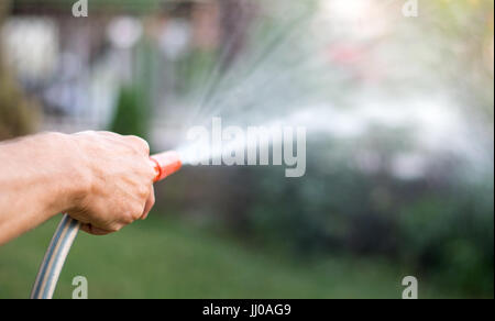 Uomo fiori di irrigazione con un tubo flessibile al di fuori Foto Stock