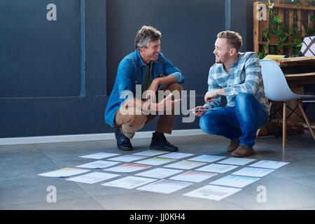 Due colleghi sorridente il brainstorming con documenti su un pavimento di office Foto Stock