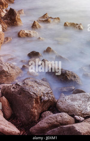 Tramonto sulla spiaggia rocciosa vicino fino Foto Stock