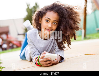 African American Girl con smart phone giacente a terra Foto Stock