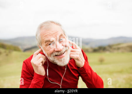 Active senior runner in natura in appoggio, ascoltando musica. Foto Stock