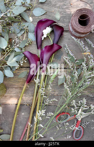 Nozze setup floreali su una panca in legno nella luce del sole con le forbici, spago, eucalipto e lillies Foto Stock