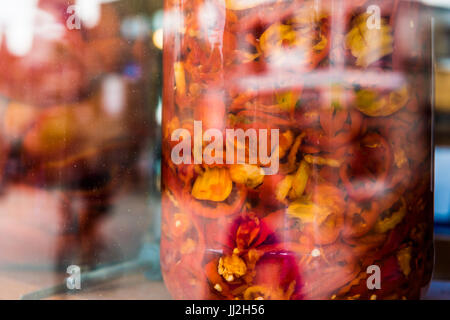 Marinata di peperoni rossi e gialli in grandi vasi sul display dietro il vetro della finestra Foto Stock