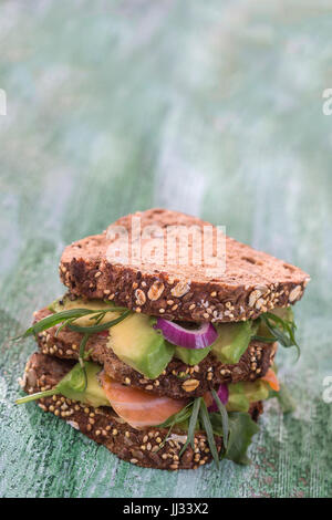 Countrybread Avocado, salmone salato sandwich con herss fresco sul verde craked paintt tavola di legno dello sfondo. Mangiare sano tema Foto Stock