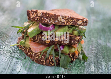 Countrybread Avocado, salmone salato sandwich con allevamenti fresco sul verde craked paintt tavola di legno dello sfondo. Mangiare sano tema Foto Stock