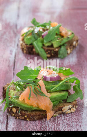 Countrybread Avocado, salmone salato sandwich con erbe aromatiche fresche in rosa craked paintt tavola di legno dello sfondo. Mangiare sano tema Foto Stock