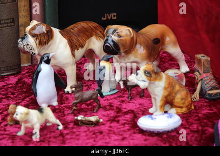 Selezione della Cina di ornamenti, cani, bulldogs e pinguini visualizzati su materiale rosso al mercato di Portobello Road Foto Stock