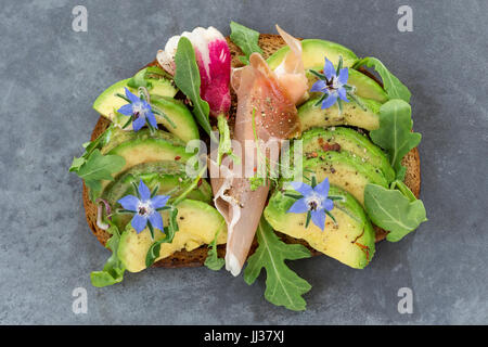 Pane integrale di Avocado, smockef panino di prosciutto con erbe fresche ,borragine, su grigio ardesia sfondo Foto Stock