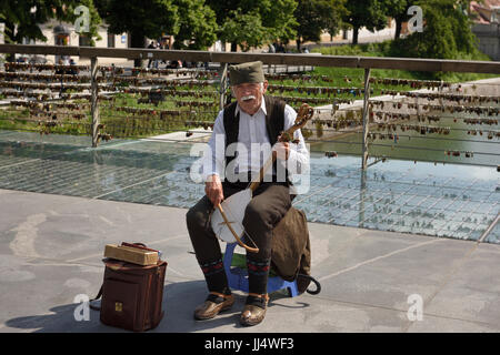 Maschio vecchio musicista di strada suonando e cantando un singolo Gusle a corda con arco sulla macelleria ponte sopra il fiume Ljubljanica Ljubljana Slovenia Foto Stock