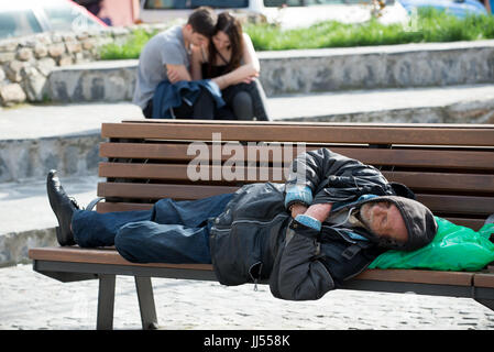 Un senzatetto di dormire su un banco pubblico a Sibiu in Transilvania, Romania Foto Stock