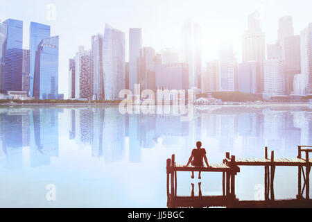 Concetto di sogno, uomo seduto sul molo e godendo di paesaggio urbano moderno skyline view Foto Stock