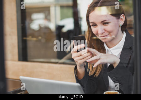 Piuttosto giovane donna caucasica utilizza lo smartphone e sorridente Foto Stock