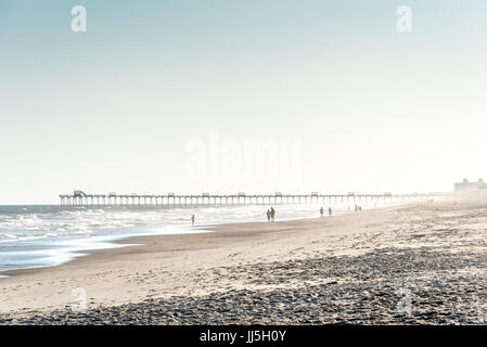 La gente che camminava sul isola di smeraldo beach w/ Boga Pier a distanza in una nebbiosa sera passeggiata sulla spiaggia, Crystal Costa della Carolina del Nord, Sud Outer Banks Foto Stock