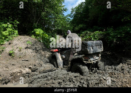 Un uomo russo guida un quad fuoristrada in un'area montuosa fangosa nel lato sud-orientale dell'isola di Sakhalin, nell'Oceano Pacifico. Russia Foto Stock