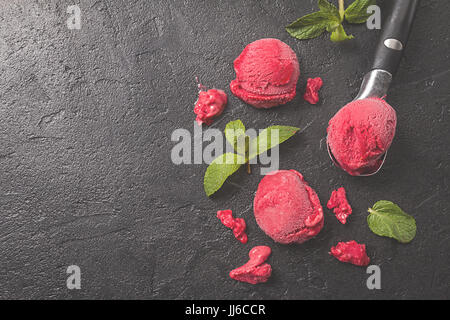 Rosso lampone gelato in palline di gelato cucchiaio con la menta su sfondo nero Foto Stock