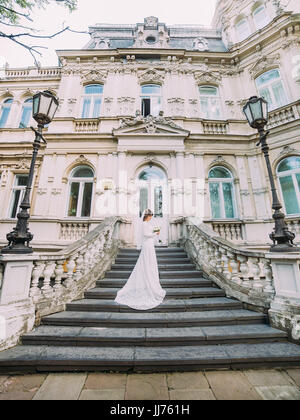 Il lato a tutta lunghezza ritratto della sposa nel lungo abito da sposa con il bouquet mentre in piedi sulle scale. Foto Stock