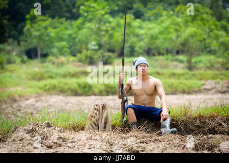 Maschio agricoltore detiene un fucile mentre è seduto su un prato. Foto Stock