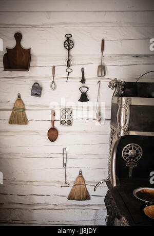 Pioneer attrezzi da cucina sono appesi alle pareti di un edificio in legno, accanto a a legna, stufa a Fort Edmonton Park, in Edmonton, Alberta, Canada Foto Stock