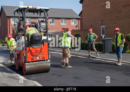 Squadra che posa Tarmac, bitmac, aspahlt e utilizzando rulli stradali in un nuovo sviluppo di case in St Anne's in mare. Tarmacadam, propriamente chiamato macadam bituminoso o 'Bitmac' per brevità, è spesso pensato per essere il metodo più economico di superficie di un viale o di un piazzale, macadam è un processo di legare insieme aggregati più piccoli, come pionierizzato dal leggendario John MacAdam nel 19 ° secolo. Lytham, Blackpool, Regno Unito Foto Stock